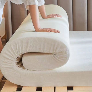 Hotel mattress topper being unrolled on a bed frame, showing thick foam with fabric cover