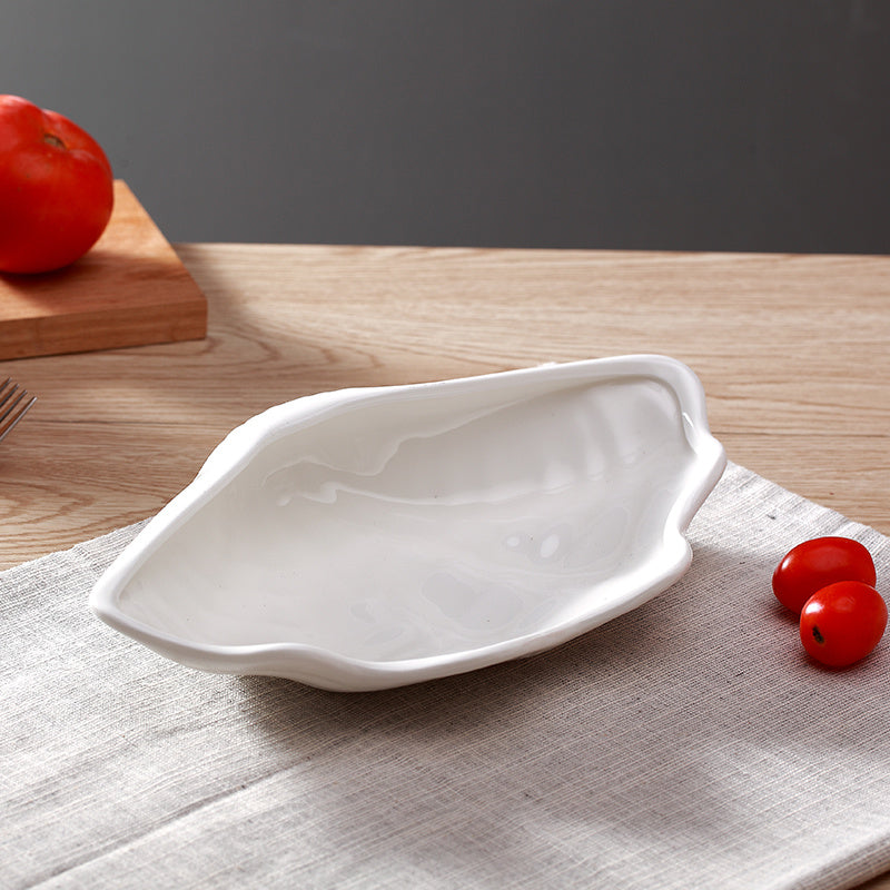 Single wavy-rimmed white ceramic shell plate resting on linen placemat beside two cherry tomatoes