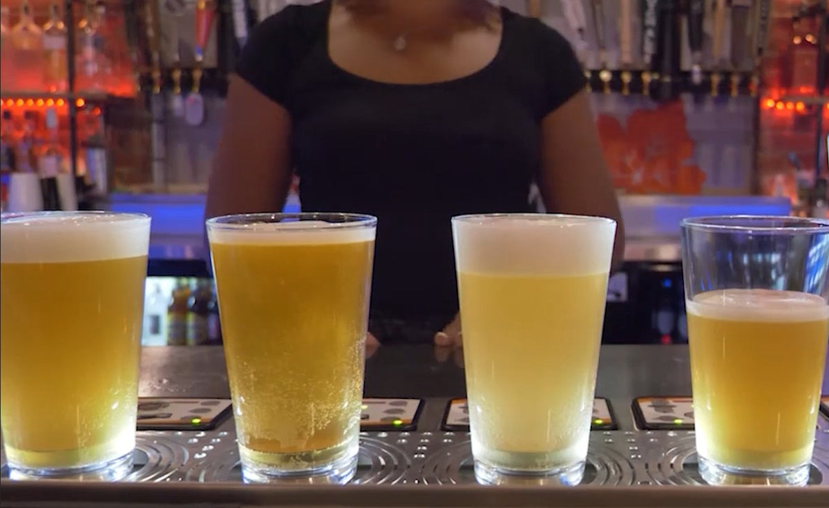 Four pint glasses filling from the base along a bottoms-up dispensing pad, bartender behind the bar