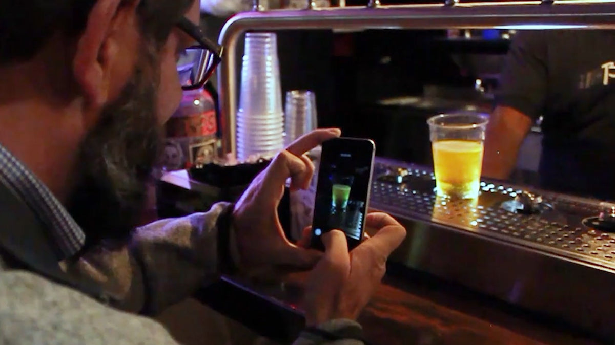 Guest filming a pint on a bottoms-up dispenser with his phone across the bar
