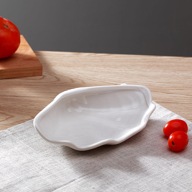 Empty white ceramic shell-shaped plate on linen placemat with two cherry tomatoes to the side