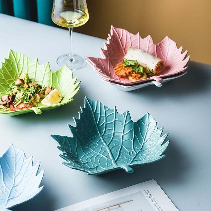 Leaf-shaped ceramic plates wholesale in green, pink, blue, and teal styled on a dining table with food