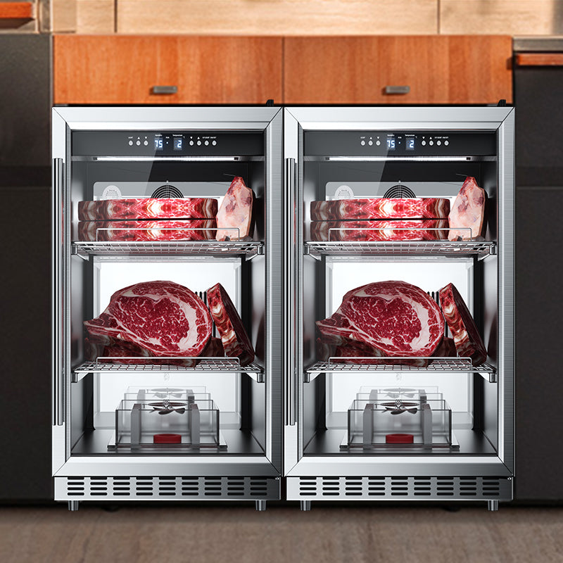 Two dry aging cabinets side by side in a kitchen island, each with glass doors, digital displays, and shelves of raw steaks a