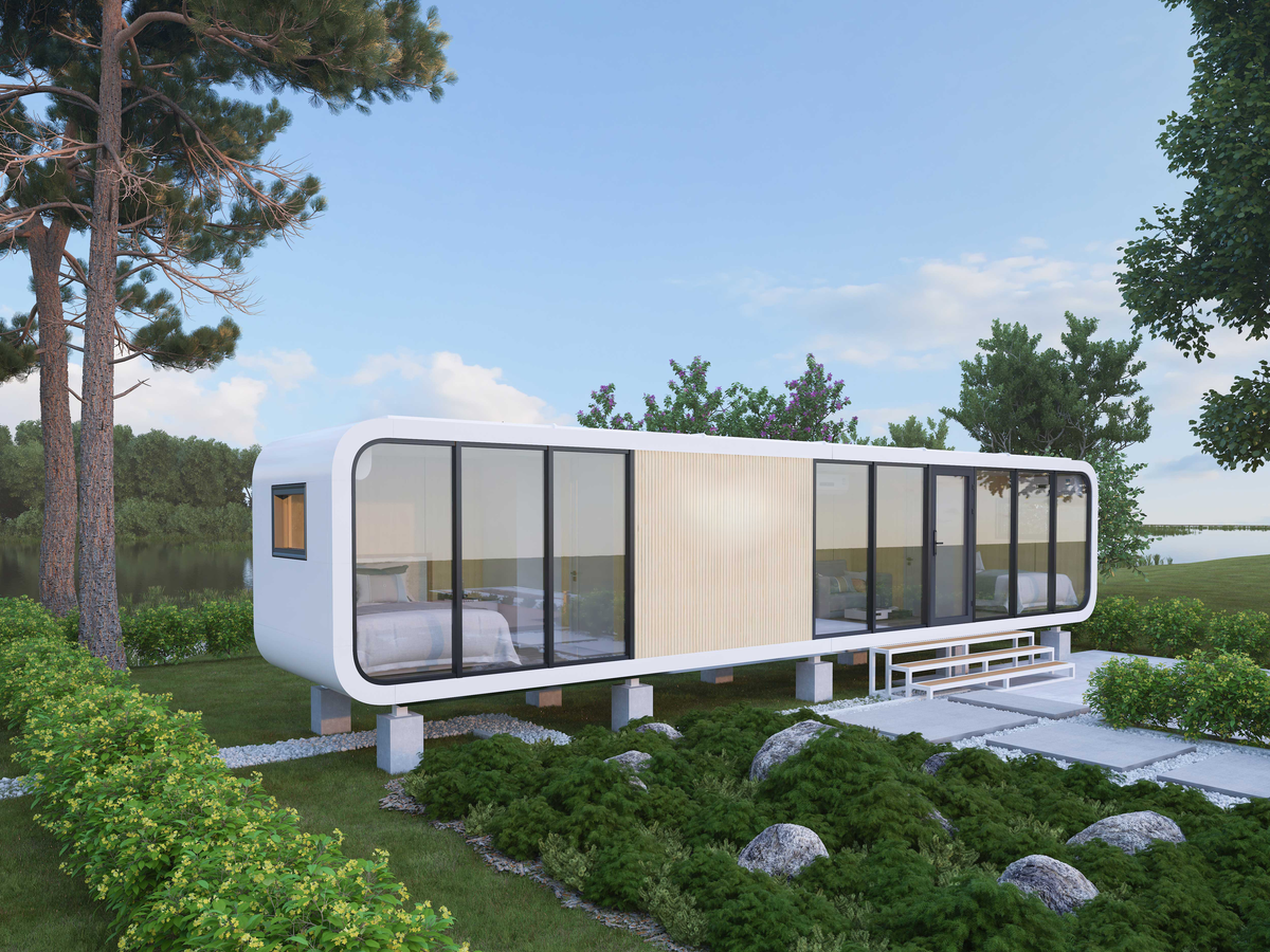 Elevated modular cabin with black-framed glass panels and wooden accent wall, set beside a lake with trees behind