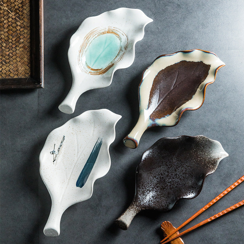 Four hand-painted leaf-shaped ceramic plates in teal, brown, black, and white glazes on dark surface