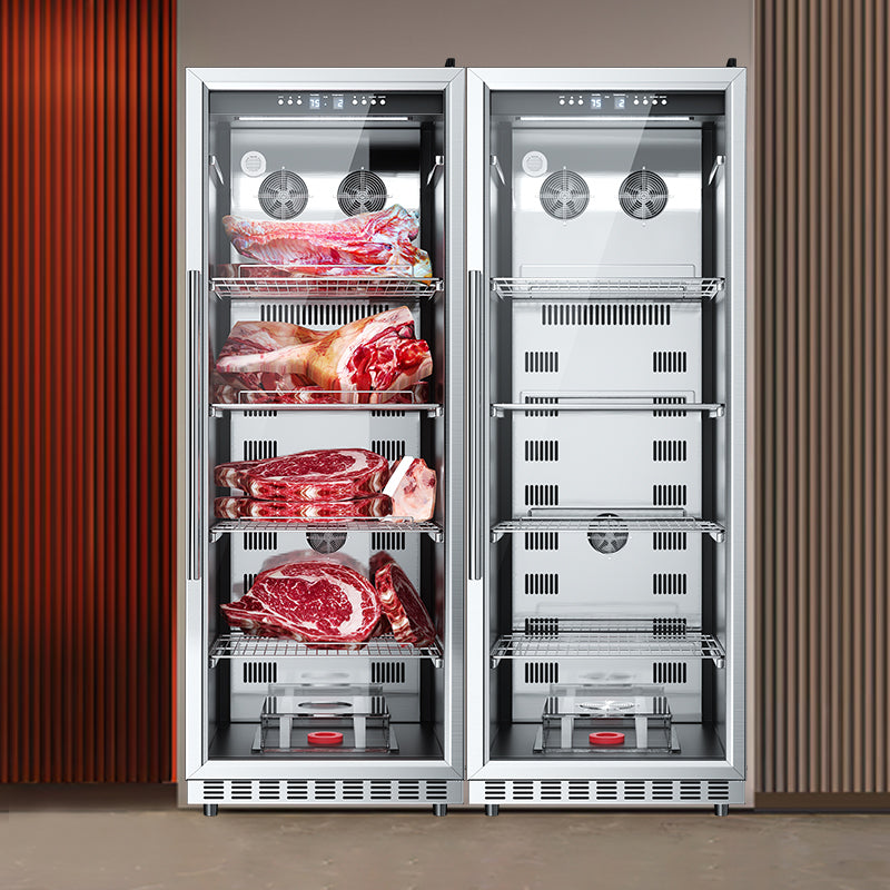 Two tall dry aging cabinets standing side by side against a wall, each with glass doors and multiple shelves loaded with raw