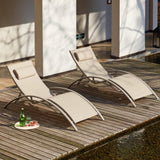 Dos tumbonas beige en forma de S sobre una tarima de madera junto al agua, con una bandeja de bebidas cerca