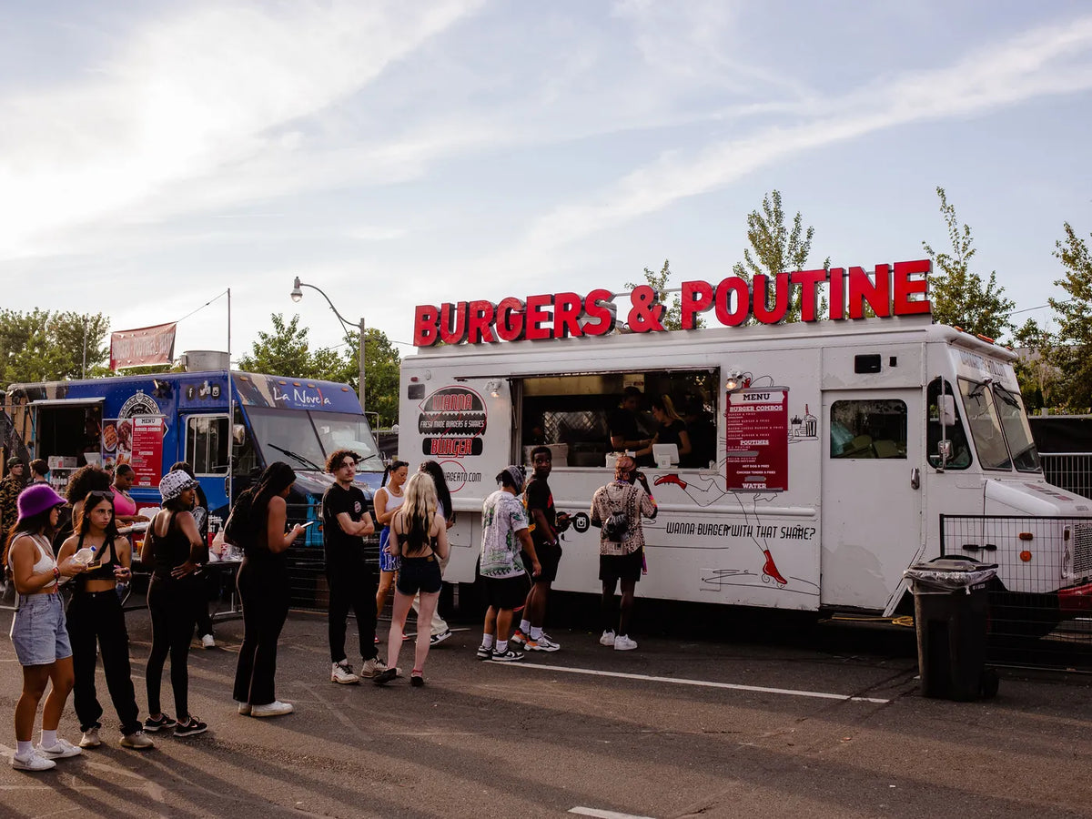 Customers queueing at the serving window of a white food truck on a sunny afternoon