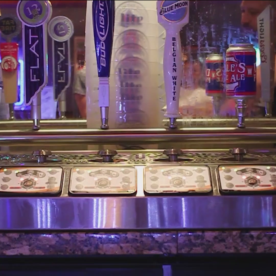 Pints filling from the base on a four-tap bottoms-up dispenser behind a busy bar