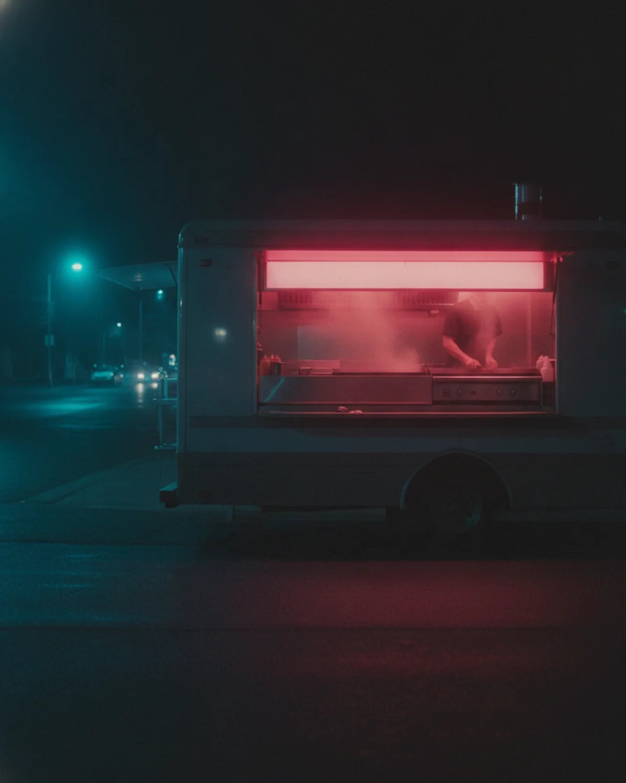 The lit serving hatch seen from the customer's side, a cook working at the griddle behind
