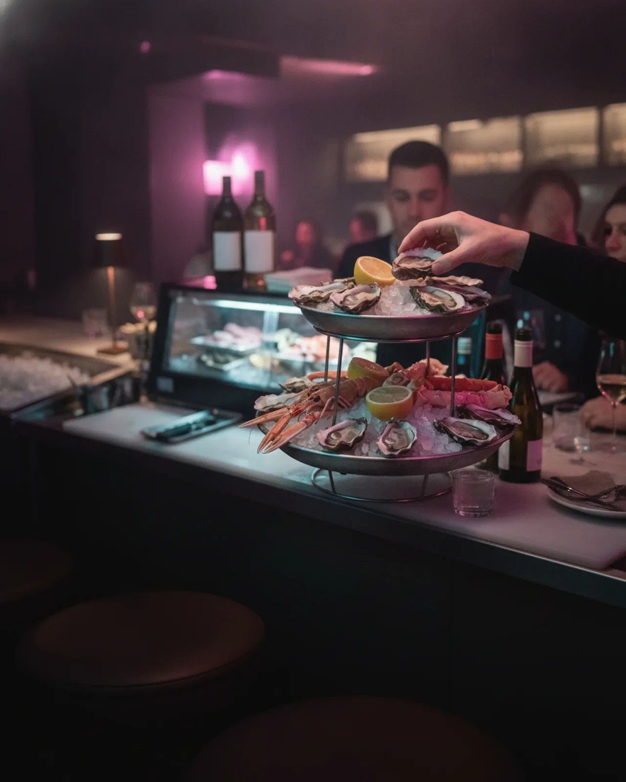 Hand setting an oyster on a two-tier seafood stand of oysters, langoustines and crab over crushed ice