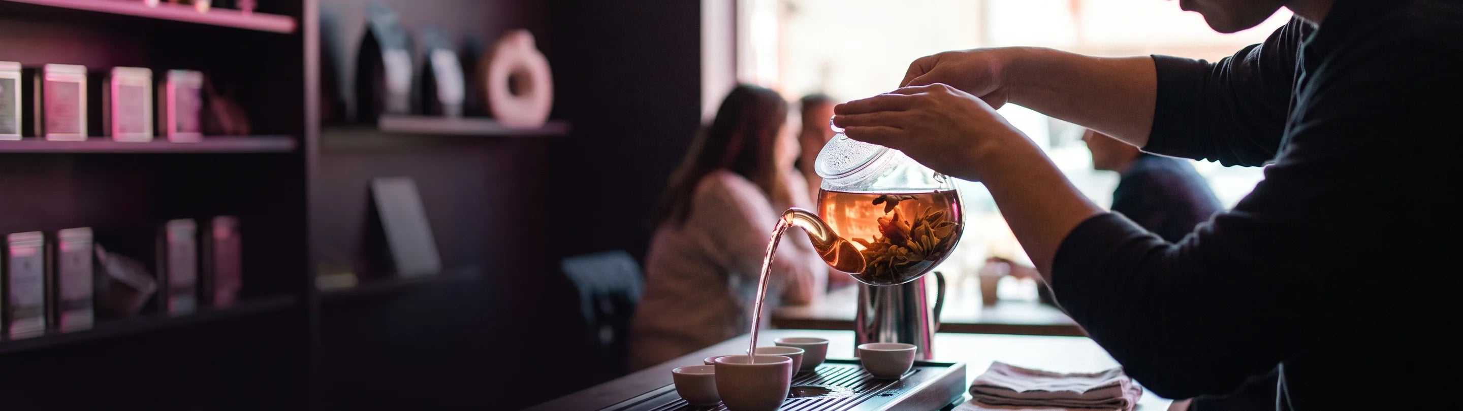 Glass teapot and cups on a wooden counter, steam rising, tea leaves in the pot